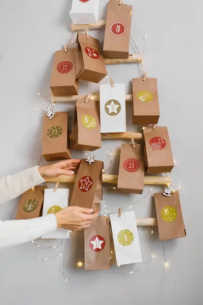 El yapımı Noel takvimini hediyelerle birlikte asmak. Anne çocuklar için festival dekoru ve geleneği hazırlıyor. Eko ağacında tarihi olan çantalar, duvarda sıfır atık, 24 Aralık için bir torba göster.
