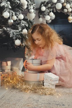 Kıvırcık kız Noel ağacının yanında hediyeler açar..