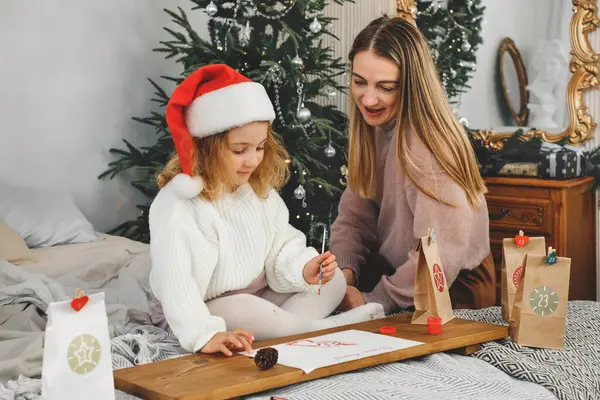 Anne ve bebek kız Noel mektubu yazıyorlar ve yatak odasında takvim işleri yapıyorlar. Evdeki çocuklar için şenlik aktiviteleri. Mutlu rüya kızı zanaat yaratıyor