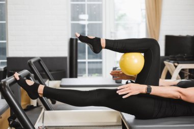 Person doing leg-up while practicing pilates on reformers with ball in studio. Legs close-up in gym,  clipart