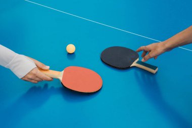 Masa tenisi raketi ve topun yakın plan çekimi. Eller, mavi masa tenisi masasının üzerinde kürekleri tutuyor. Spor konsepti. Pankart