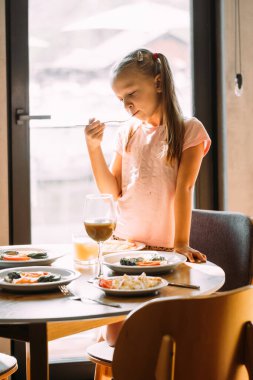 Genç kız modern otelde kahvaltıdan hoşlanıyor. Tabaklar taze sebze, yumurta ve içeceklerle dolu.