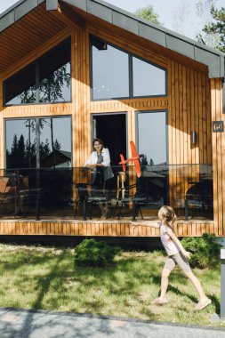 Anne ve kızı modern bir otel kabininde kaliteli vakit geçiriyorlar. Ahşap evin yanında kızla ve kırmızı oyuncak uçakla oynayan bir kadın. Tatil ve aile seyahatleri yazın açık havada. Etkin dinlenme
