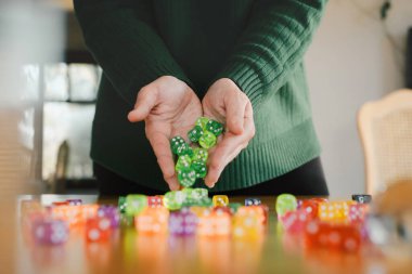 Kadın ellerinde zar. Masa oyunları konsepti. Sarı masanın üzerinde renkli oyun aksesuarları var. Uzayı kopyala Yeşil zarları kadınların ellerinde toplayın, heyecan verici bir eğlence için hazırlanın.