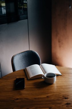Ahşap masa, açık bir kitap ve mutfakta beyaz bir fincan kahve. Rahatlama ve rahat anlar için mükemmel bir yer.