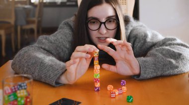 Parlak oturma odasında masa üstü oyunu sırasında renkli zar yığını inşa eden kadın. Mutlu gülen kadın evde oyun oynamaktan hoşlanıyor.