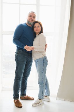 40 'lı yaşlarda sevgili bir çift büyük pencerenin önünde birlikte güzel vakit geçirmenin tadını çıkarıyor. Aile gülümsemesi, sarılma, sevinç anı ve birliktelik. 