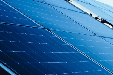 Yenilenebilir enerji üretimi için kurulmuş güneş panellerinin detaylı yakın plan görüntüleri. Paneller bir ızgaraya yerleştirilmiş, güneş ışığını yakalayarak elektriğe dönüştürüyorlar. Yeşil enerji, sürdürülebilirlik 