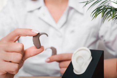 Modern dijital işitme cihazları odiyologların elinde klinikte. Doktor işitme cihazını tutuyor. Uyum ve gösteri için kulak modelinin yanında. Yakın plan.