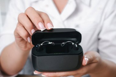 Doktorlar ellerinde iki dijital işitme cihazı olan açık bir dava tutuyorlar. Sağlık ve günlük kullanım için modern asistanlık teknolojisi