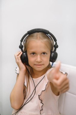 Odiyometri kabinindeki gülen kız kulaklık takıyor ve klinikteki çocuk işitme testi sırasında ses tonlarına tepki veriyor.