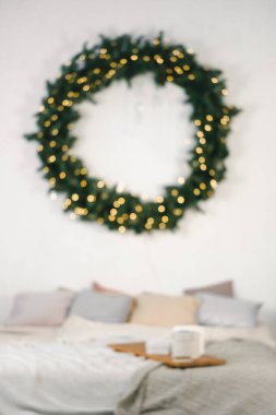 Bulanık Minimalist yatak odası Noel için büyük yeşil bir çelenk, peri ışıkları, rahat yastıklar ve yatağın üzerinde tatil hediyeleri ile süslenmiş. Arkaplan 