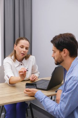 Kadın otolargolog, klinikteki orta yaşlı hastaya modern minyatür işitme cihazları ve profesyonel tıbbi danışma seti gösterdi.
