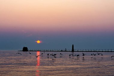 Batan bir güneş, Grand Haven, Michigan, rıhtım ve deniz fenerinin üzerinde gökyüzünün yumuşak tonlarını değiştiriyor. Yüksek kalite fotoğraf
