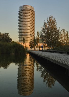Bir su kütlesinin yanındaki bankta oturan bir insan.