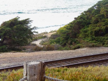 Okyanus kıyısına giden tren raylarını geçen bir kum yolu..