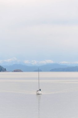 Arka planda dağlar olan sakin sularda giden bir gemi.