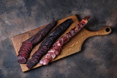 İki parça füme sığır eti ve sosis, arka planda kesim tahtasının üzerinde.