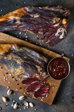 İki kuzu bacağı tütsülenmiş ve koyu arkaplanda tahta bir tahta üzerinde dilimlenmiş.