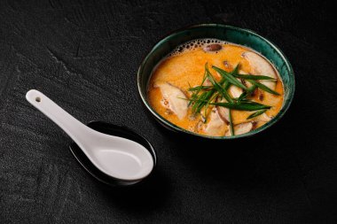 Tom yum kung soup with mushroom and spoon on black bacground. National dish of Laos and Thailand.