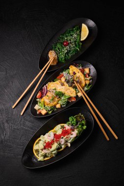 Chuka wakame, Cesare salad and Avocado salad and chopsticks in Japanese stile on a black concrete background. Top view