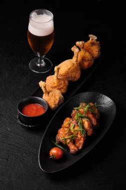 Fried chicken legs, Sweet sauce chicen wings and a glass of beer on black concrete background