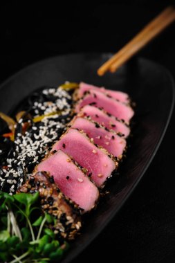 Baked tuna served with black noodles on black concrete background