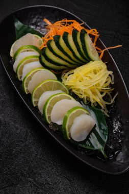 Scallop sashimi with vegetables on black concrete background
