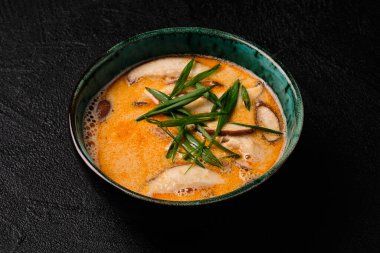 Tom yum kung soup with mushroom and spoon on black bacground. National dish of Laos and Thailand.