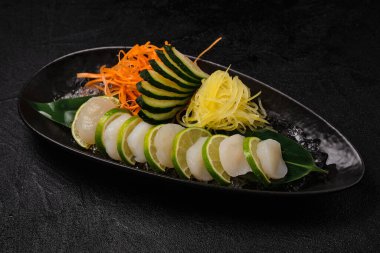 Scallop sashimi with vegetables on black concrete background