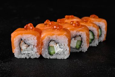salmon sushi roll with red caviar on top on black concrete background