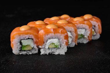 salmon sushi roll with spicy sauce on top on black concrete background