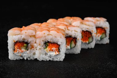 Shrimp sushi roll with cucmber and red caviar on black concrete background