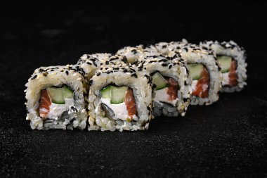 Sushi roll with salmon and cucumber inside on black concrete background