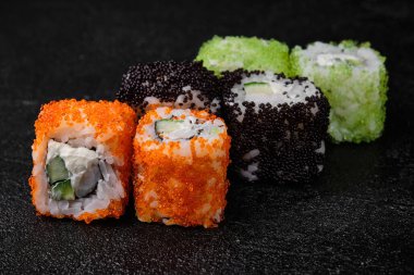 sushi roll with shrimp inside and flying fish roe on top on black concrete background