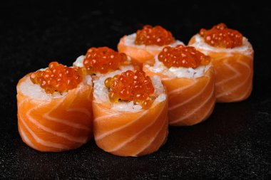 salmon sushi roll with red caviar on top on black concrete background