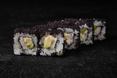 Sushi roll with shrimp inside and black flying fish roe on top on black concrete background