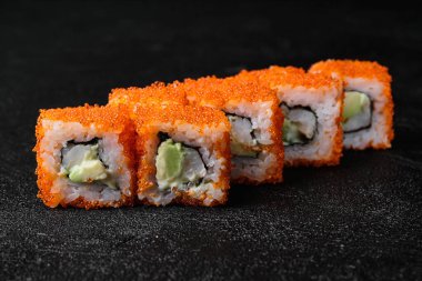 Sushi roll with shrimp inside and red flying fish roe on top on black concrete background