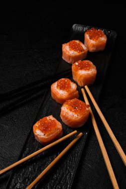 salmon sushi roll with red caviar and chopsticks for three person on top on black concrete background