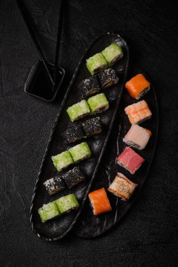 Different kind of sushi roll, soy sauce and chopsticks on black concrete background