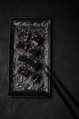 Black sushi roll on black plate on black background. Top view