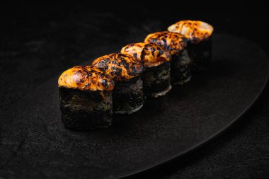 Sushi roll with baked sauce on top on black concrete background