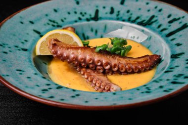 Cream soup with octopus on blue plate on black concrete background