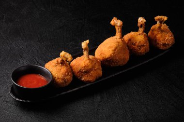 Deep-fried chicken legs and tomato sauce on black plate on black concrete background