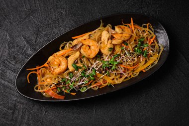 Stir-fried yakisoba noodle with shrimps and chicken on black concrete background. Asian food style. Top view