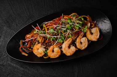 Stir-fried yakisoba noodle with vegetable and shrimps on black concrete background.  Asian food style. Top view