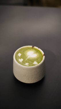 Sıcak yeşil çay lattesi, kalpli ya da ahşap arka planda bir fincanda latte sanatı seven. Metnin ya da kopyan için boşluk olan kenar görünümü, lezzetli ve sıcak