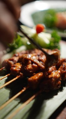 Tatlı soya soslu Sate Ayam (Tavuk satay) (Kap Manis). Endonezya 'nın popüler sokak yemeklerinden biri. Tahta masada muz yaprağı tabağında servis ediliyor. Seçici odak.