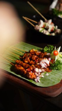 Tatlı soya soslu Sate Ayam (Tavuk satay) (Kap Manis). Endonezya 'nın popüler sokak yemeklerinden biri. Tahta masada muz yaprağı tabağında servis ediliyor. Seçici odak.