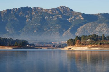 Beniarres rezervuarının iklim değişikliği nedeniyle kuraklık içindeki manzarası, Muro de Alcoy üzerindeki sabah sisi ve arka plandaki Sierra de Mariola doğal parkı. İspanya